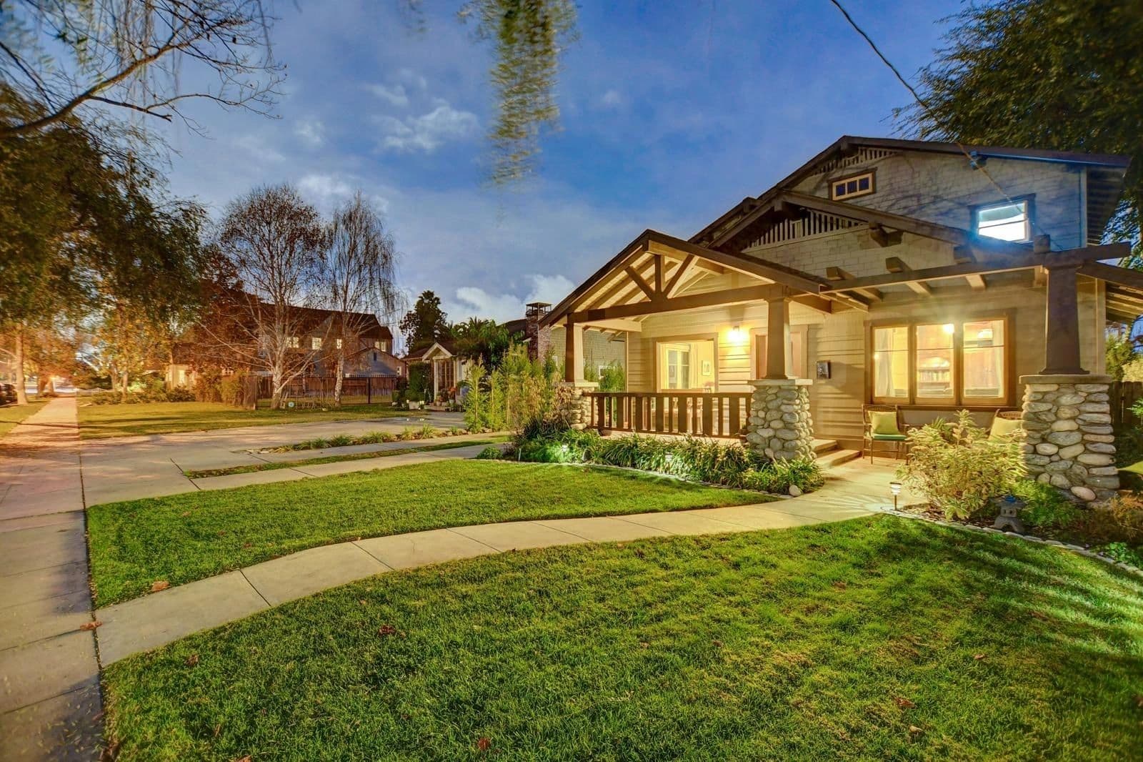 Craftsman home with a lit front porch on a tree-lined Claremont street at dusk